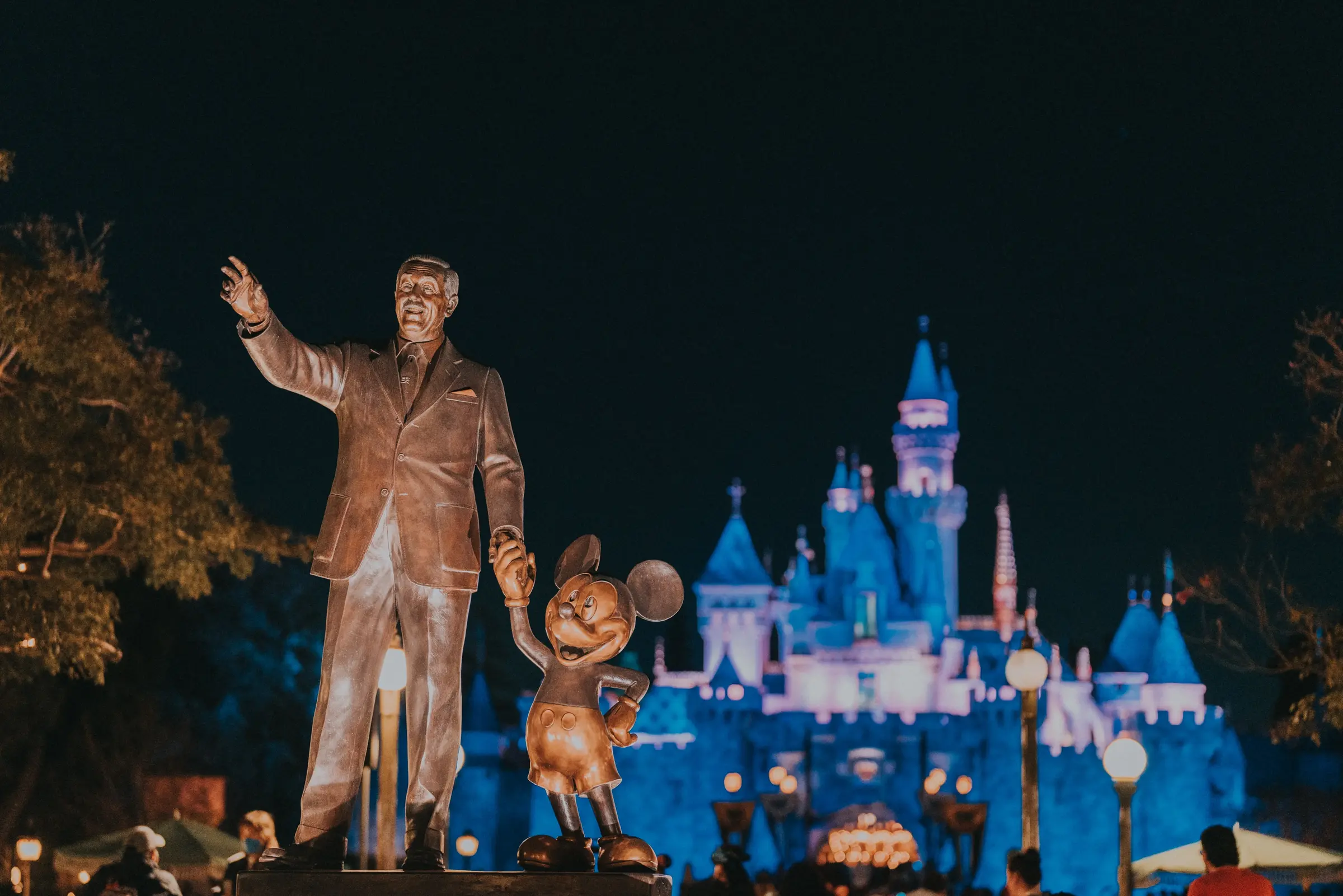 Walt Disney and Mickey Mouse statue with Sleeping Beauty Castle glowing at night