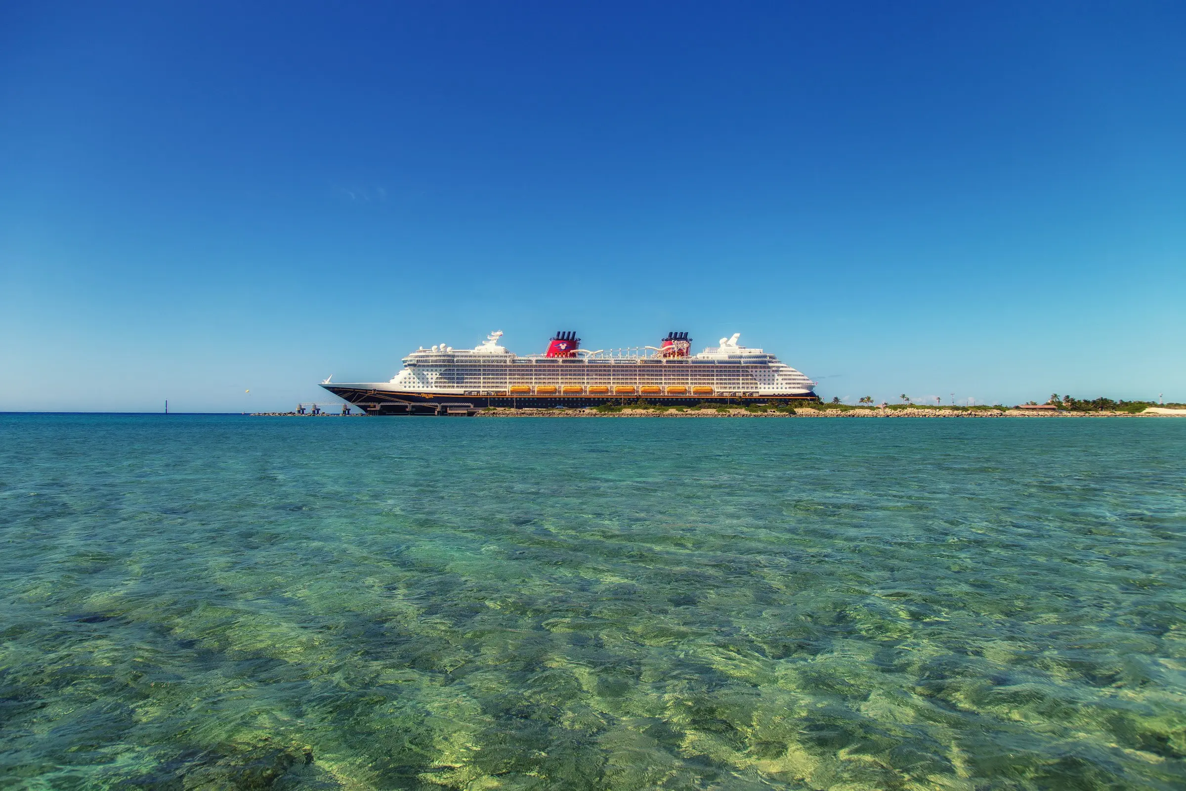 Ocean cruise ship beside clear tropical water under a brilliant blue sky