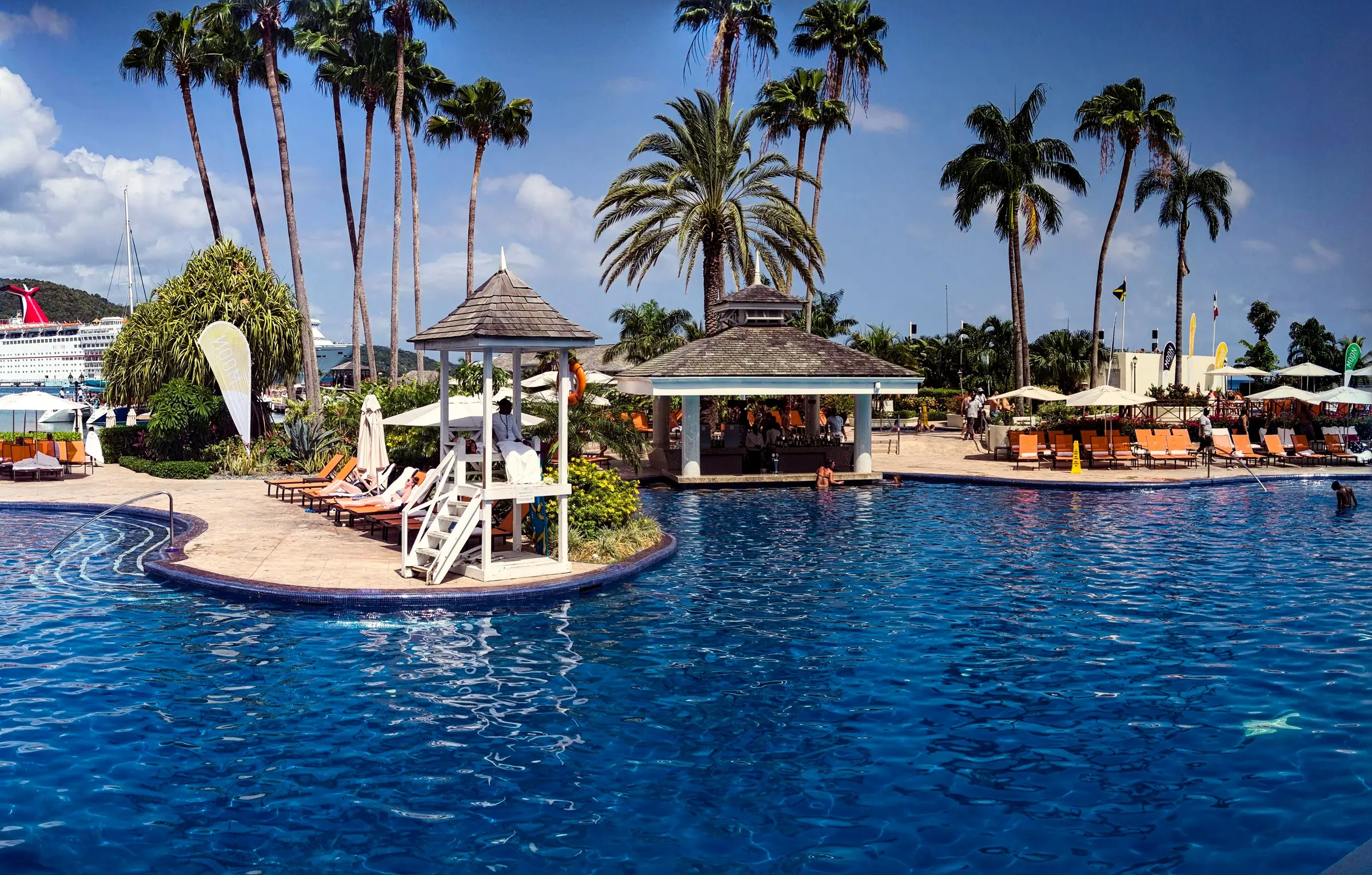 Sunny tropical resort pool with palms and a poolside gazebo